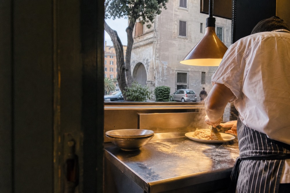 A chef plating fresh pasta in an open restaurant kitchen