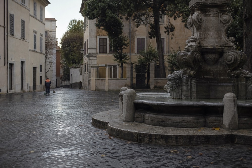 Empty Trastevere square in early morning light with fountain and closed shutters