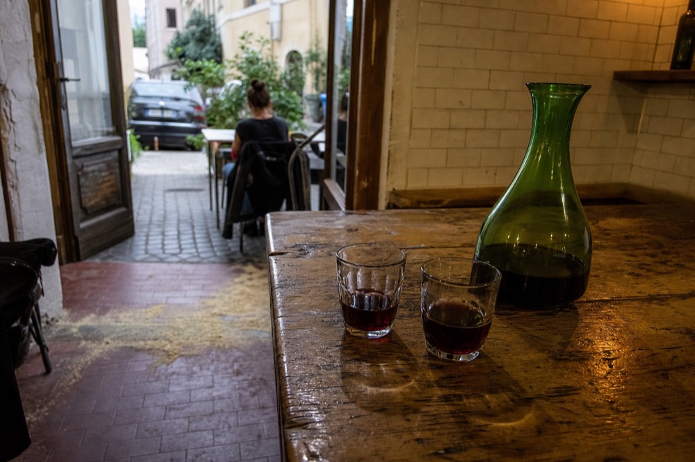 Small glasses of red house wine and a carafe on a wooden osteria counter