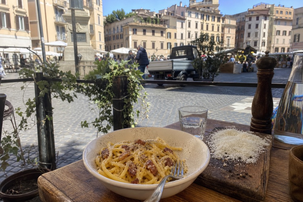 A bowl of spaghetti carbonara with guanciale and black pepper on a rustic table