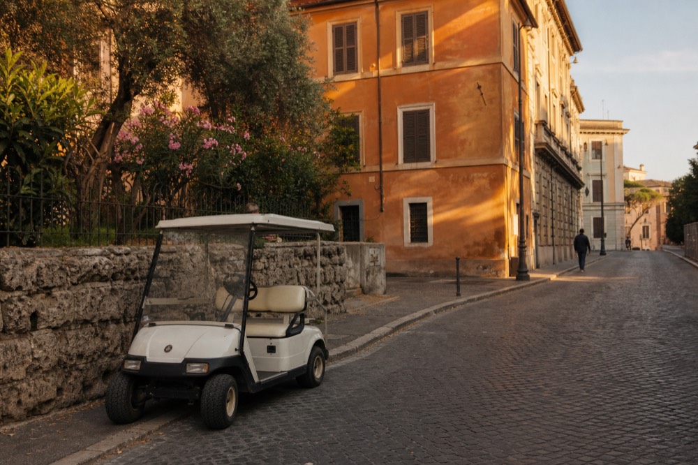 A small golf cart parked on a quiet Roman street beside a stone wall