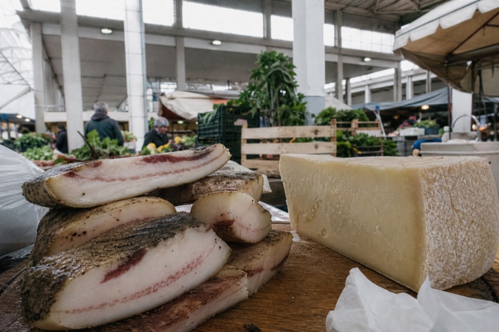 Cured guanciale sliced on a wooden board beside a wedge of pecorino cheese