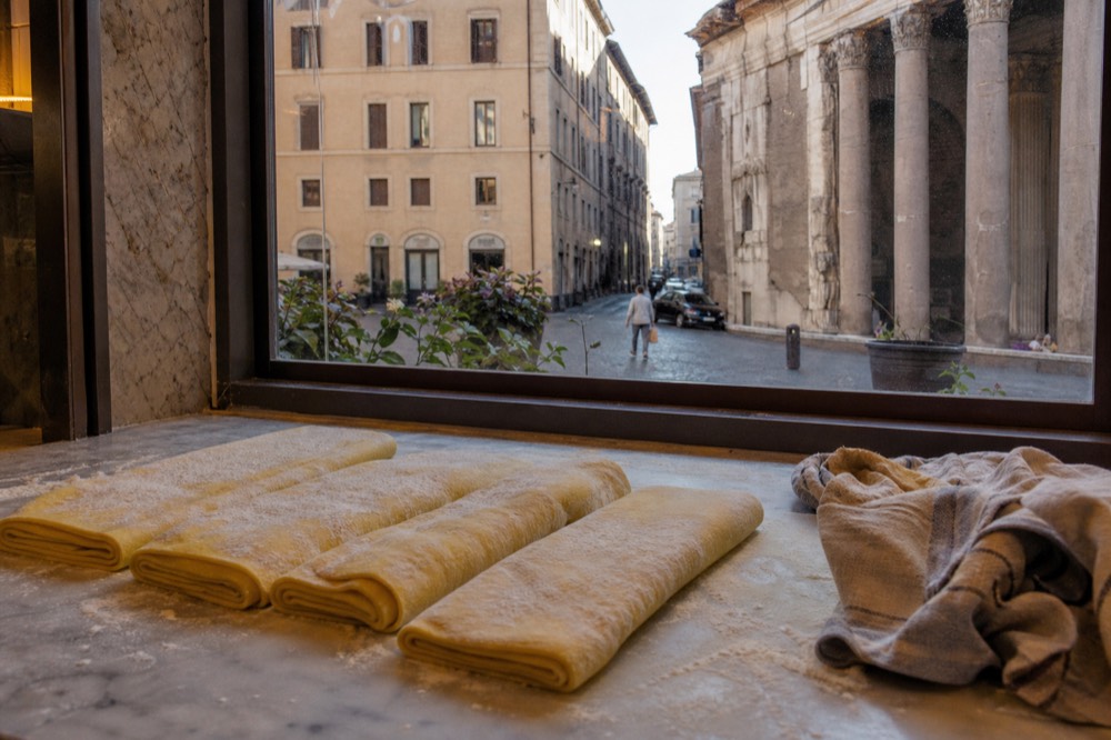 Rolled sheets of fresh egg pasta dusted with flour on a marble counter