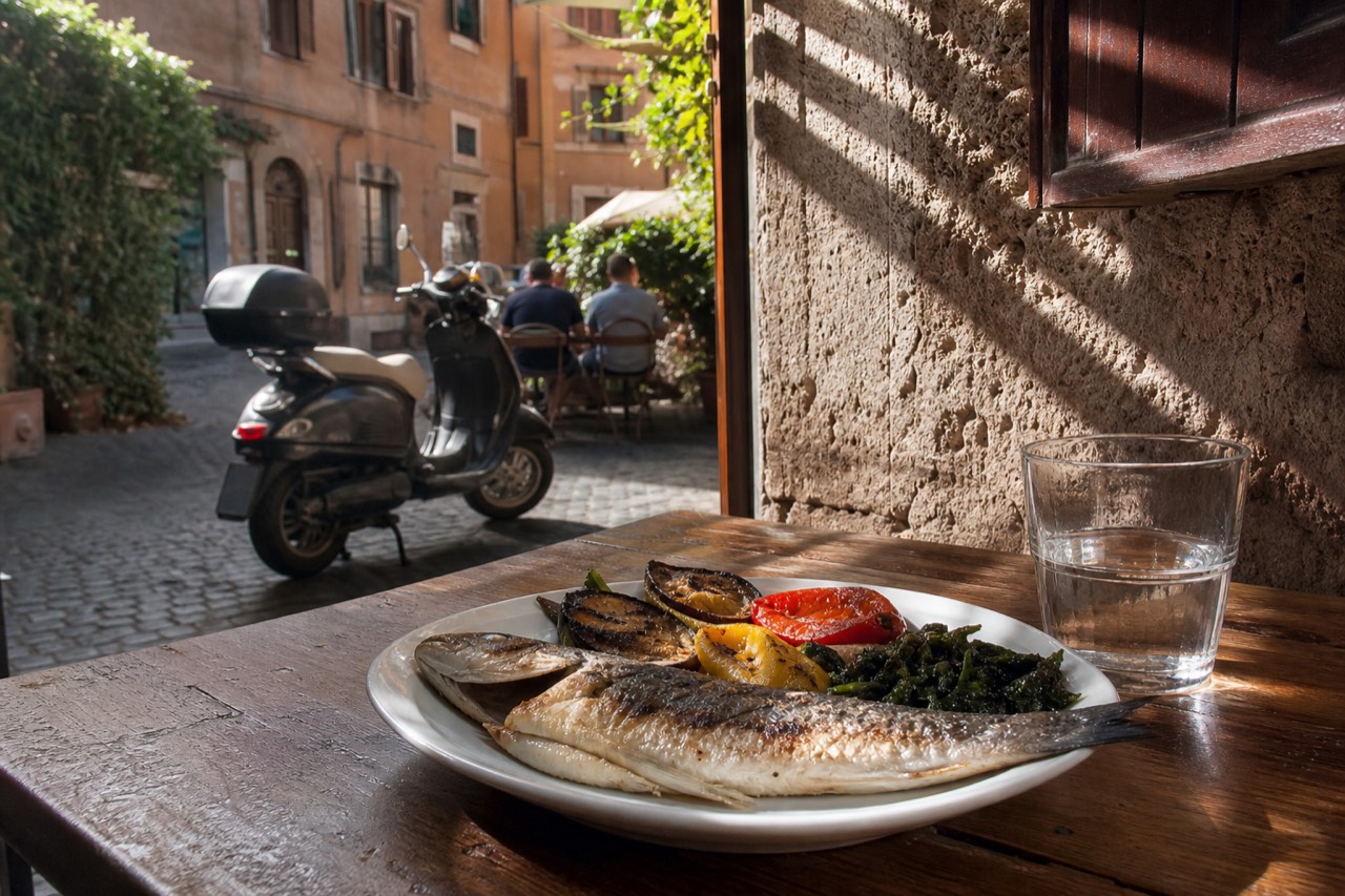 Grilled sea bass with roasted vegetables and greens on a restaurant table