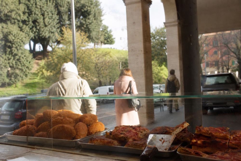 A Roman street food counter with fried snacks and pizza slices displayed in a glass case
