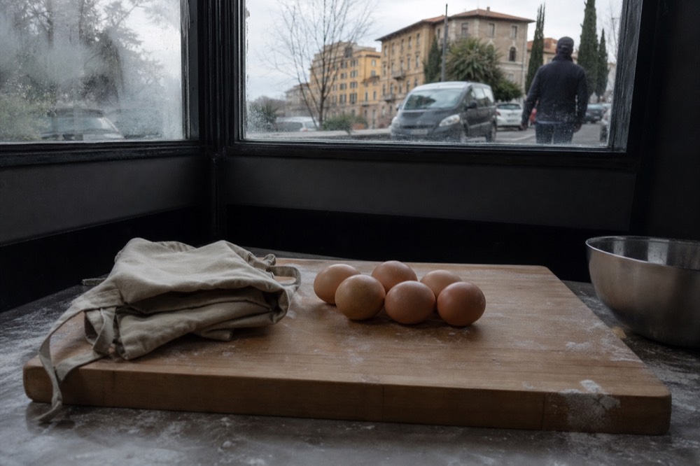 A cooking station with a folded apron, wooden board and fresh eggs ready for a pasta lesson