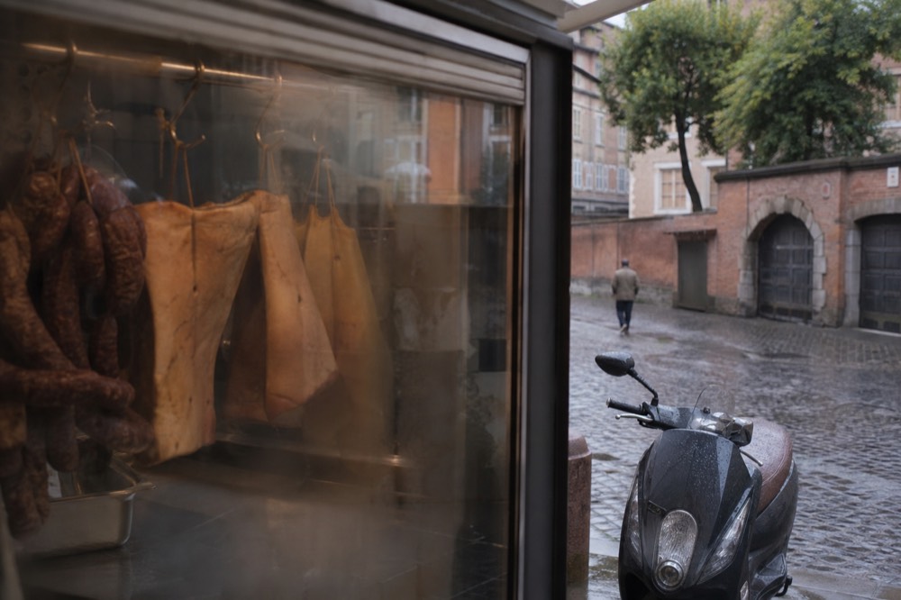 A butcher's display case with hanging cured pork jowls and salami in a Roman shop