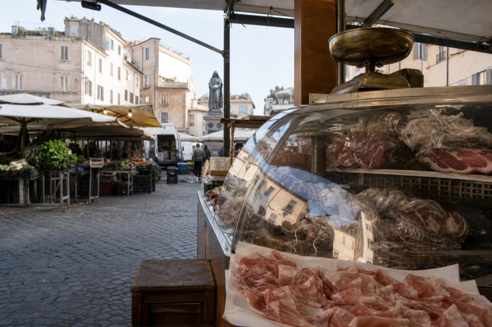 A market stall in Rome with cured meats sliced to order under a glass counter