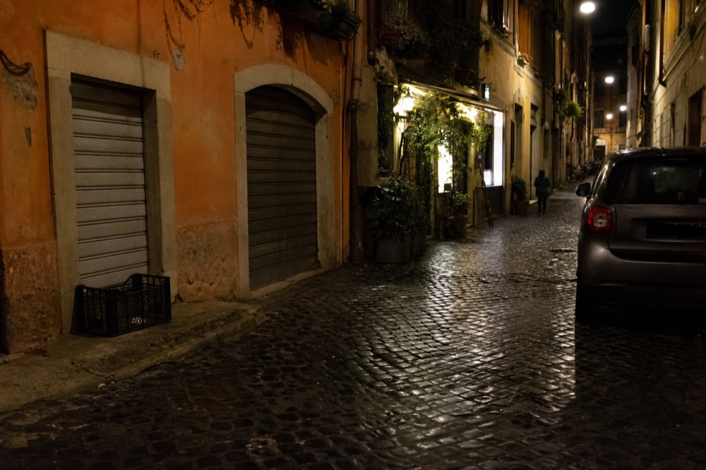 Evening street with closed minimarket shutters and lit bar windows