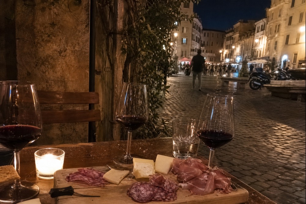 A wooden board of cured meats, cheese and glasses of red wine on a restaurant table