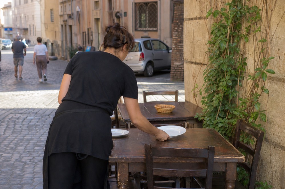 A server setting plates on a wooden restaurant table in Rome