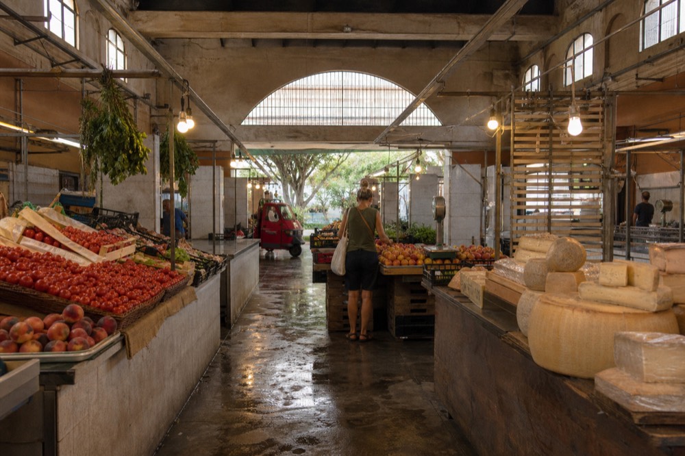 Stalls of vegetables and cheese wheels inside a covered Roman market
