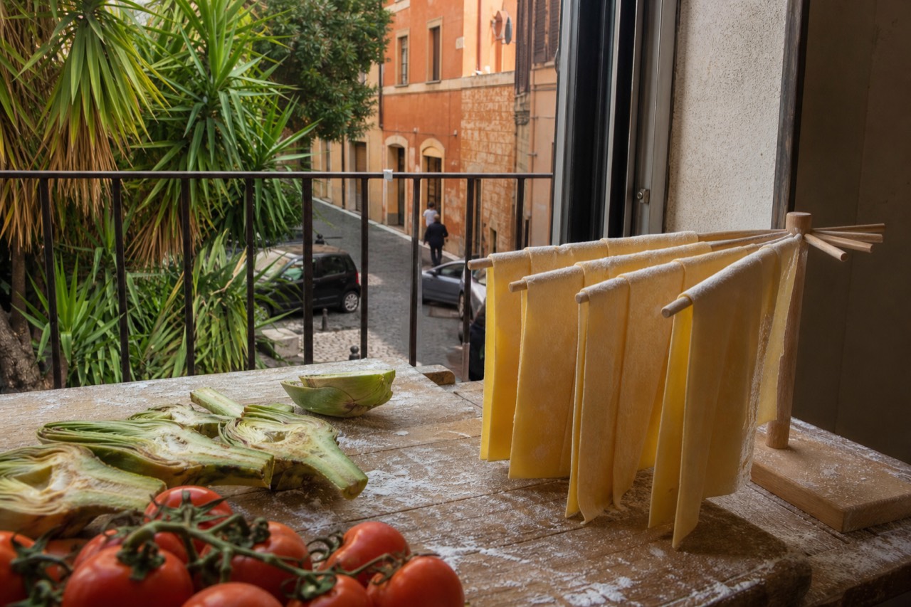 Fresh gluten-free pasta sheets and vegetables on a wooden counter in a Roman kitchen