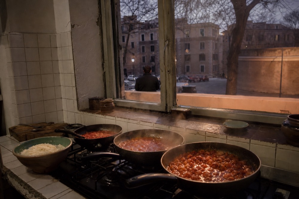 A home kitchen counter with three pans of pasta sauce simmering and a bowl of grated pecorino