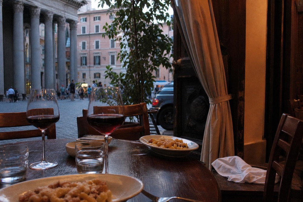 A table set for dinner with wine glasses, plates of fresh pasta and a chalkboard menu