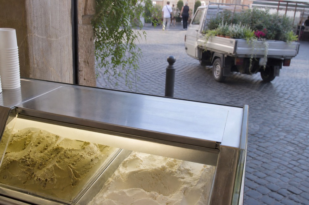 Close view of covered stainless steel gelato tins with flat, level gelato surfaces in a display case