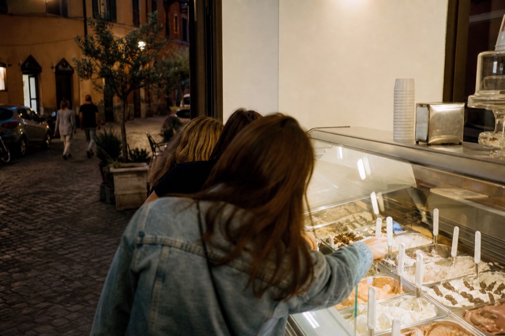 Gelateria counter on a Rome evening street with customers choosing flavors