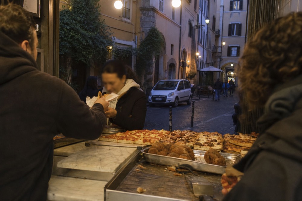 Guided food tour group sampling at a Trastevere counter, no text, no logos, no people