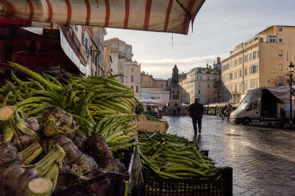 A close view of grilled Roman artichokes and fresh vegetables on a market stall counter