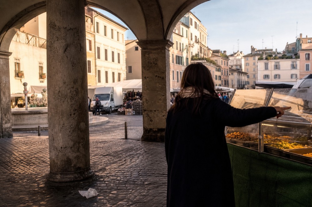 A guide pointing out fresh vegetable dishes at a Roman street food stall