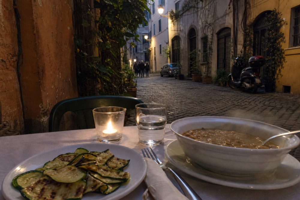 A plate of grilled vegetables and a bowl of legume soup on a restaurant table