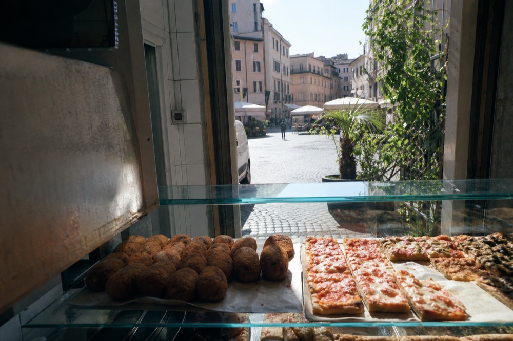 A Roman street food counter with suppli and pizza al taglio displayed in a glass case
