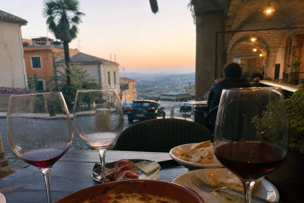 Glasses of red wine and small tasting plates on a wooden table in a Roman wine bar