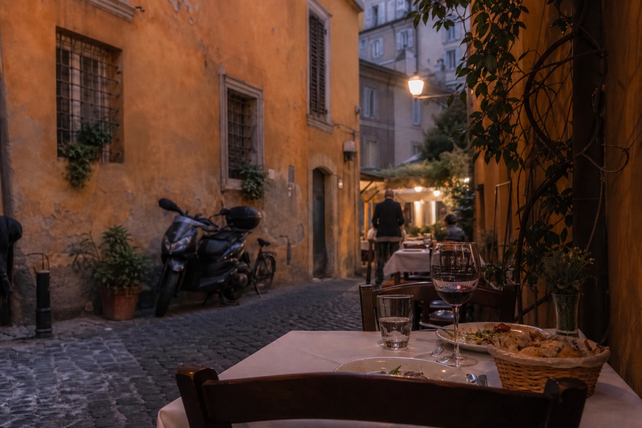 Evening tables outside a trattoria on a cobbled lane in Trastevere, Rome, with warm lamplight over the street